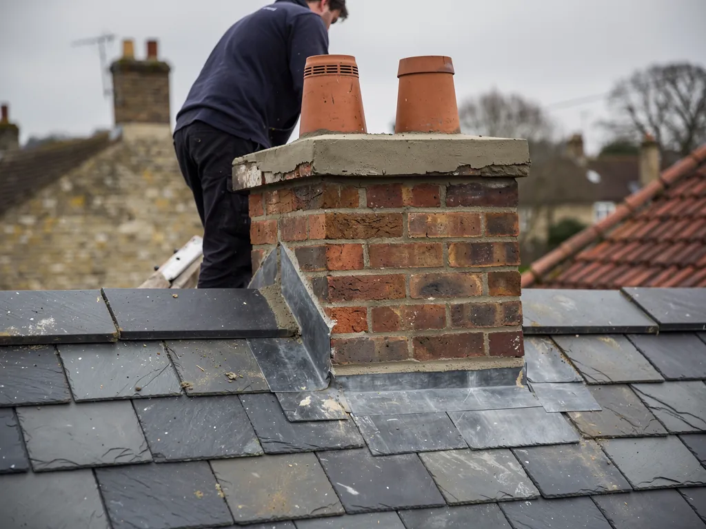 Roofer behind a brick chimney with fresh flaunching around two pots