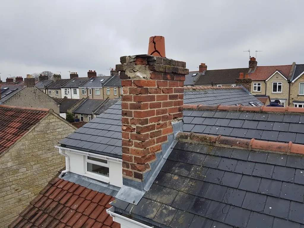 Weathered brick chimney stack with eroded joints and cracked pot