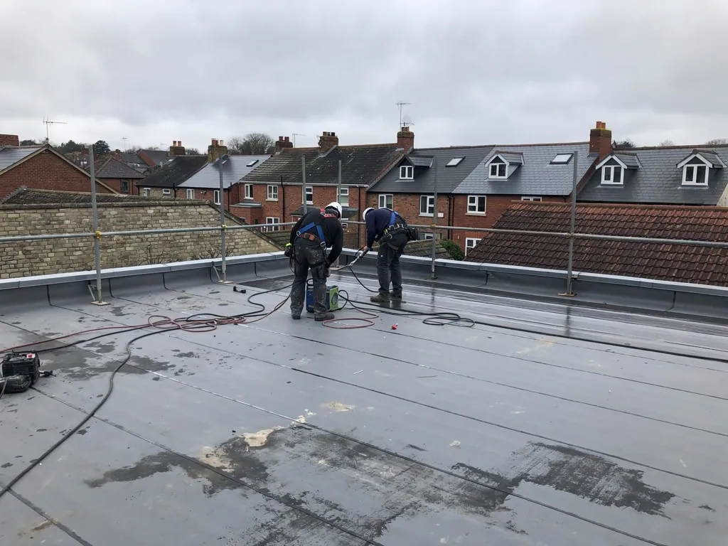 Roofers welding single-ply membrane seams on a commercial roof