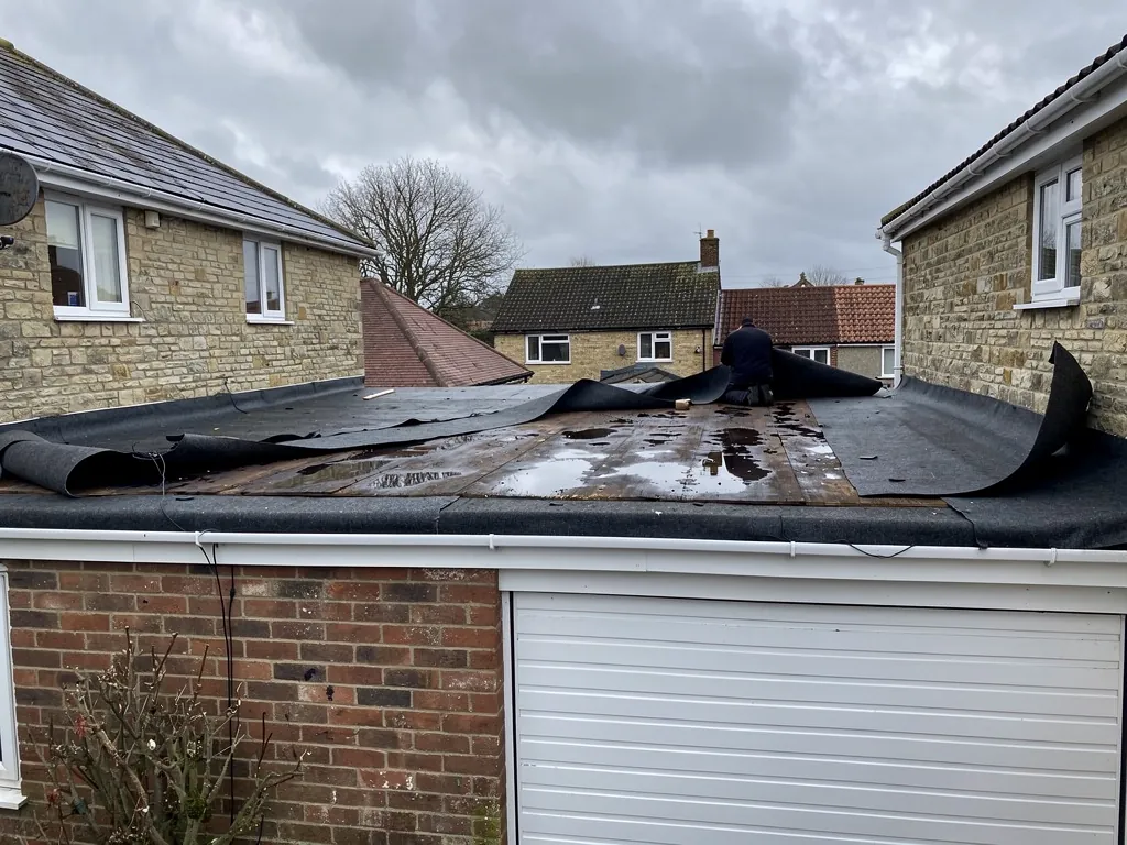 Wind-torn membrane peeled back from a wet flat garage roof