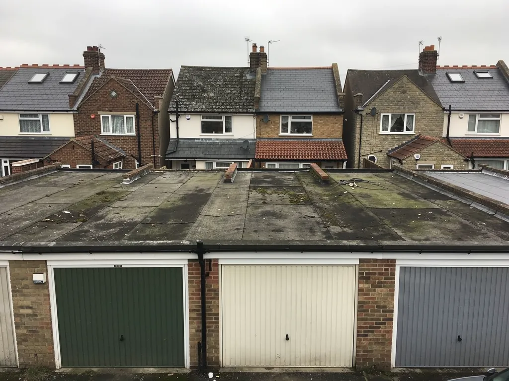Row of flat-roofed brick lock-up garages with worn felt
