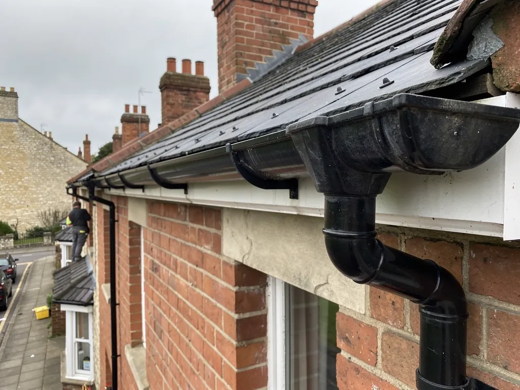 Black gutter and downpipe on the eaves of a brick terrace