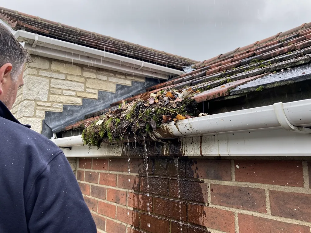 Blocked gutter full of leaves overflowing down a brick wall