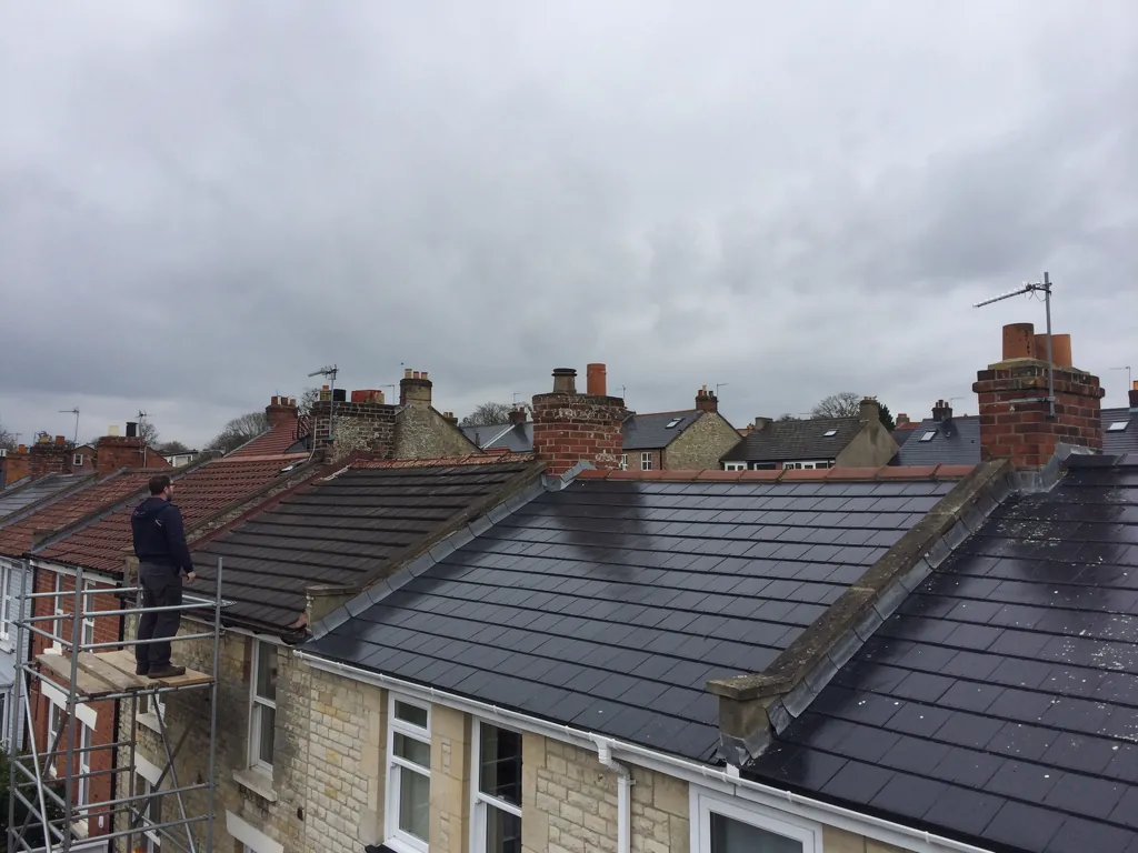 Roofer on scaffold beside a newly completed slate roof