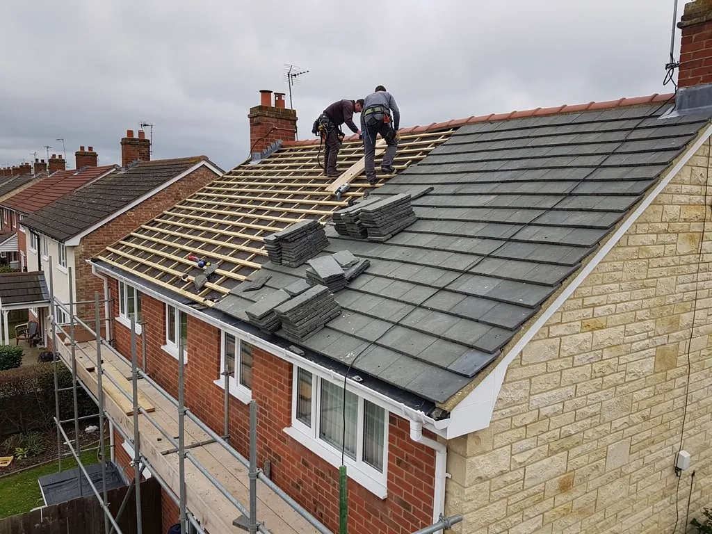Two roofers fitting grey tiles on a part-battened house roof
