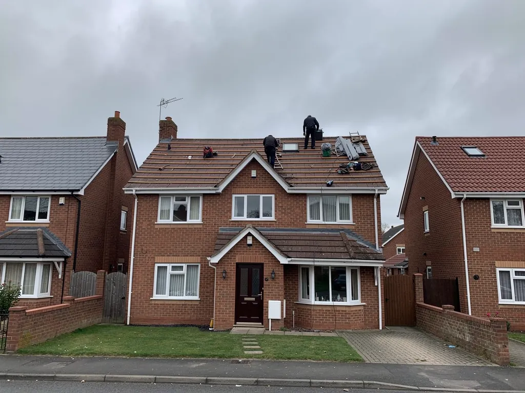 Roofers on the brown tiled roof of a 1990s brick house