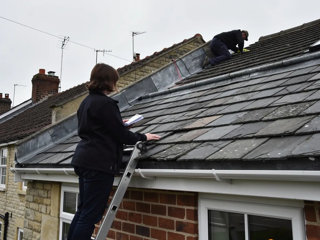 Surveyor on a ladder checking slates with a notebook