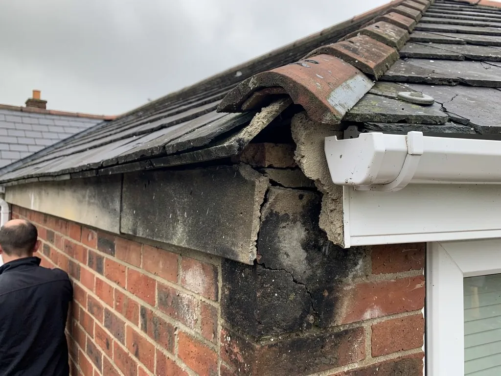 Crumbling mortar and cracked brickwork at a tiled roof eaves corner