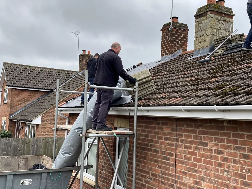 Roofer sending old tiles down a rubbish chute into a skip