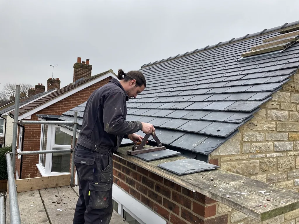 Roofer trimming a natural slate with a cutter on scaffolding