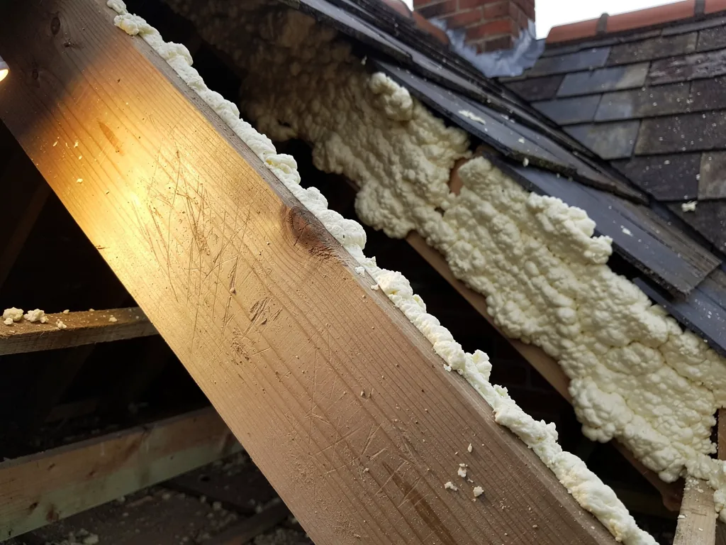 Scraped-back rafter beside thick spray foam under a slate roof