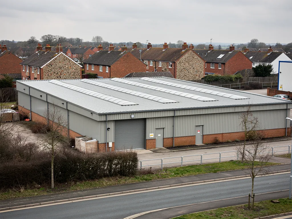 Grey profiled metal roof on an industrial unit beside housing