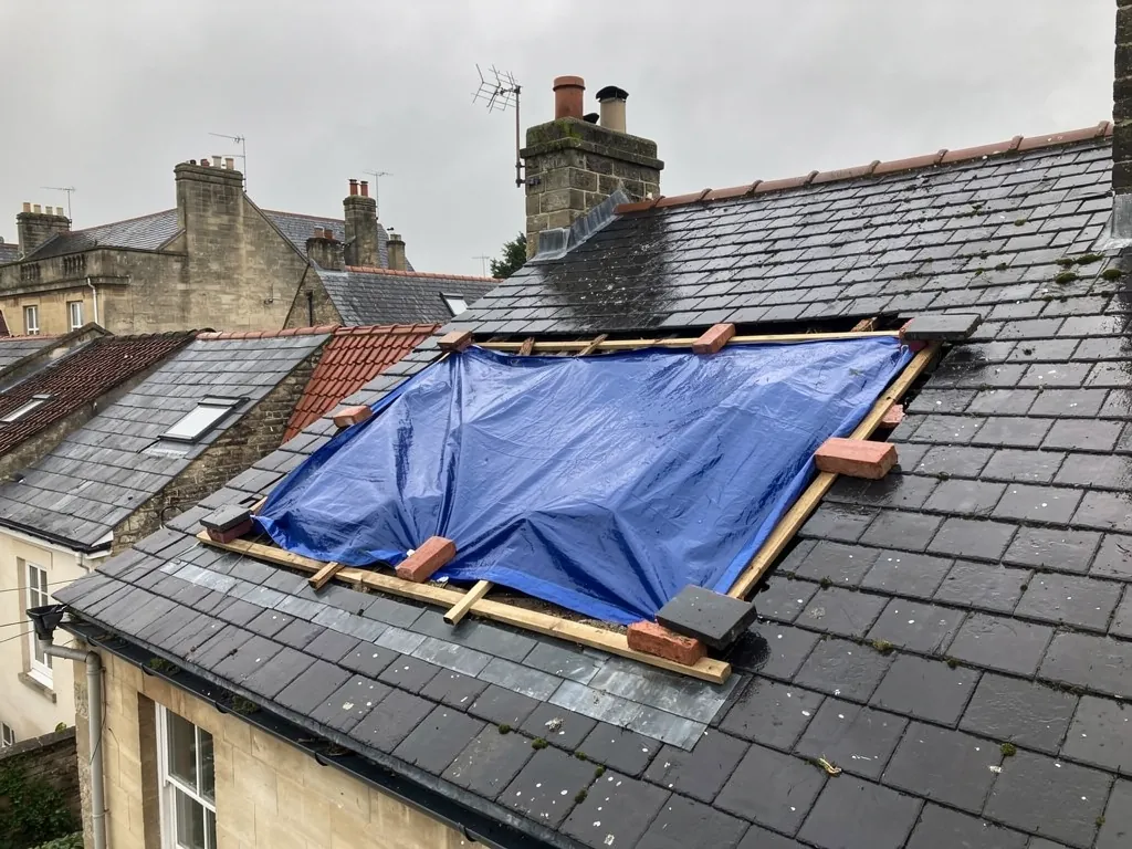 Blue tarpaulin battened over a damaged section of slate roof