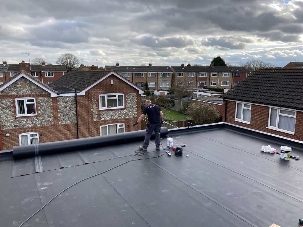 Roofer laying EPDM rubber membrane across a flat roof