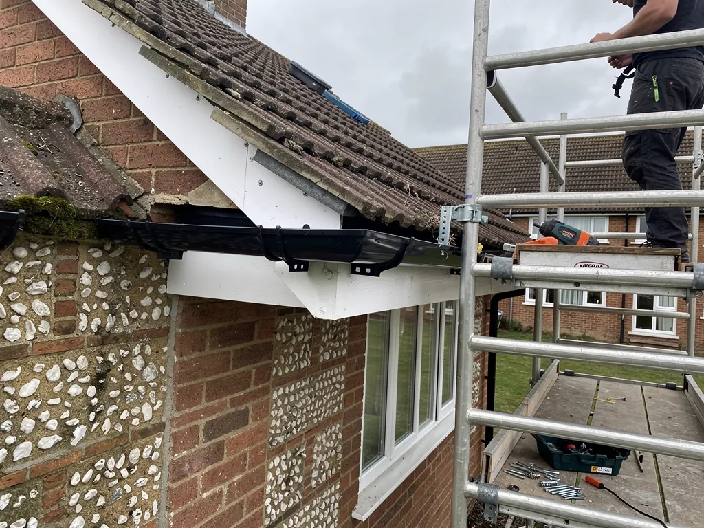 Roofer on a tower scaffold fitting new gutter and fascia