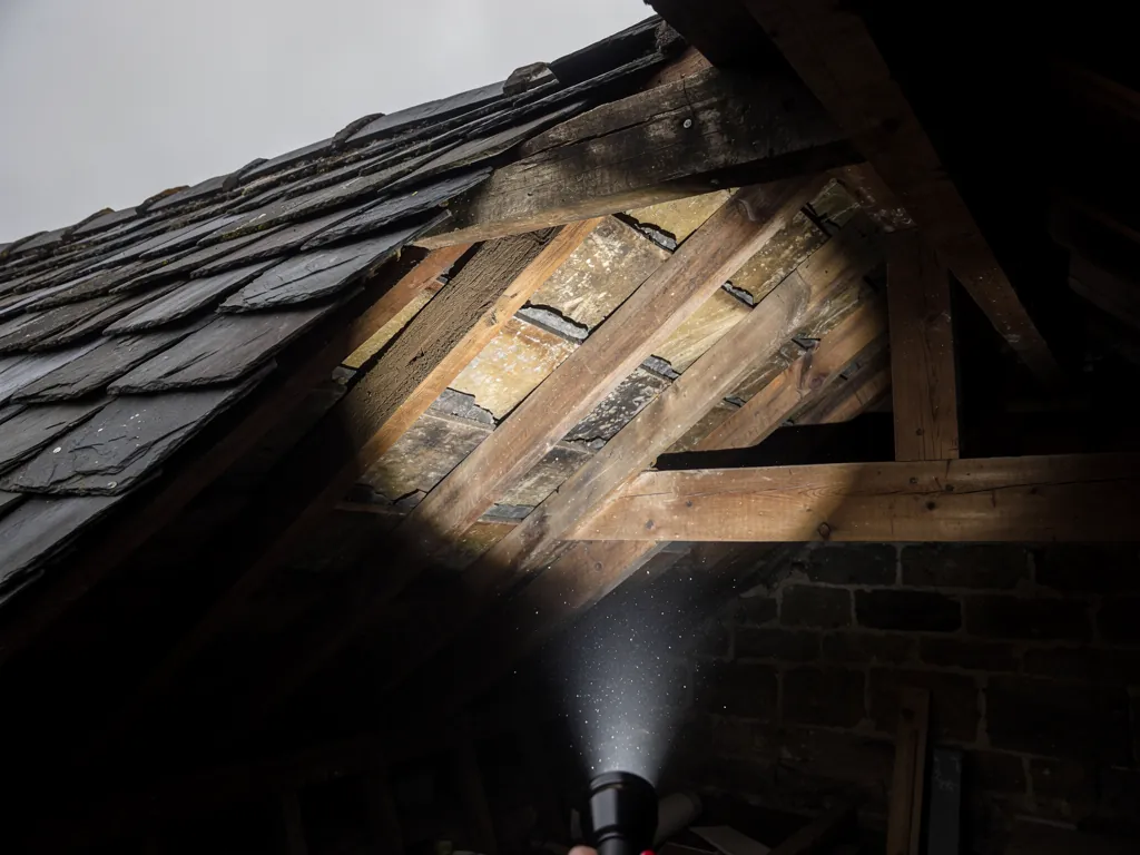 Torch beam lighting slate undersides and timbers in a loft