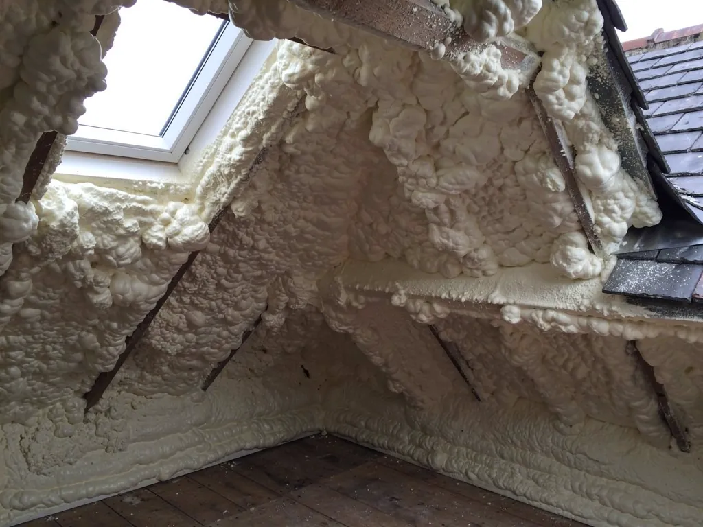 Loft thickly coated in white spray foam around a roof window