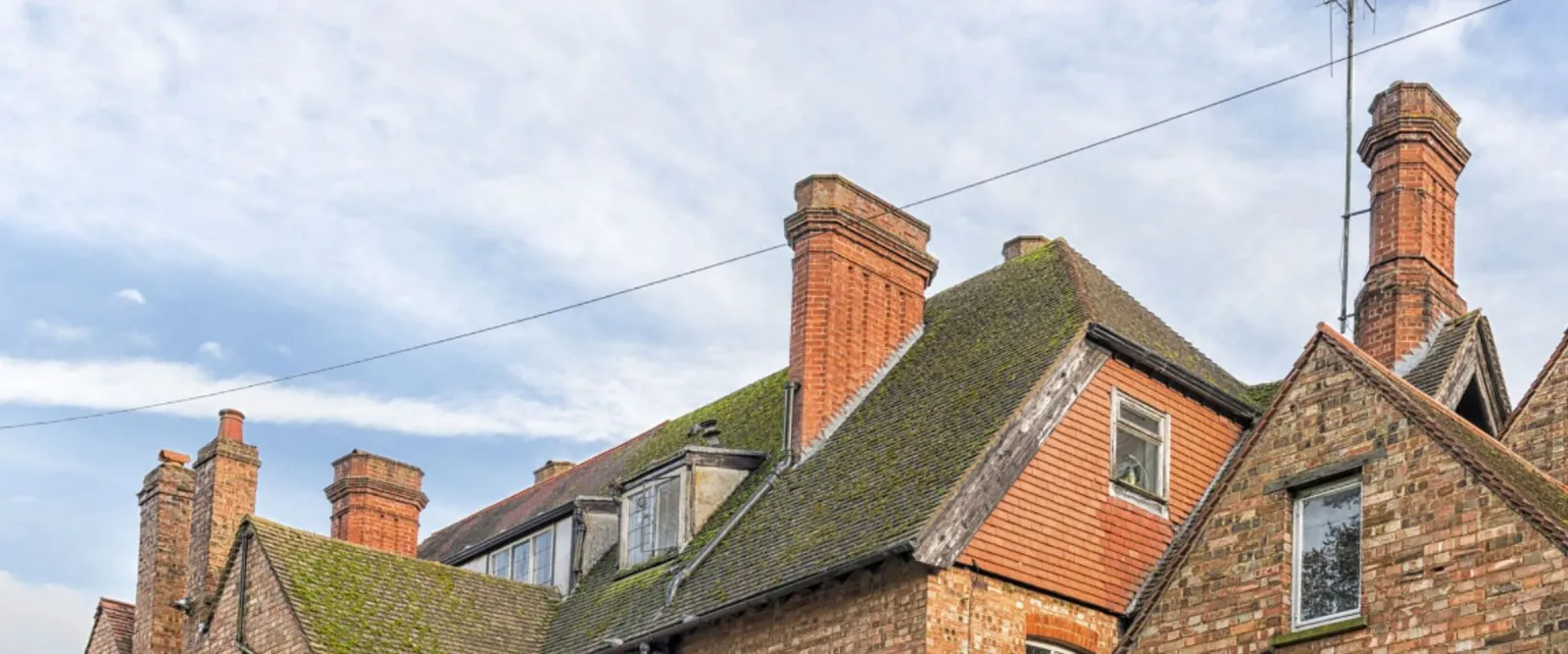 Tall brick chimney stacks rising from a mossy plain tile roof