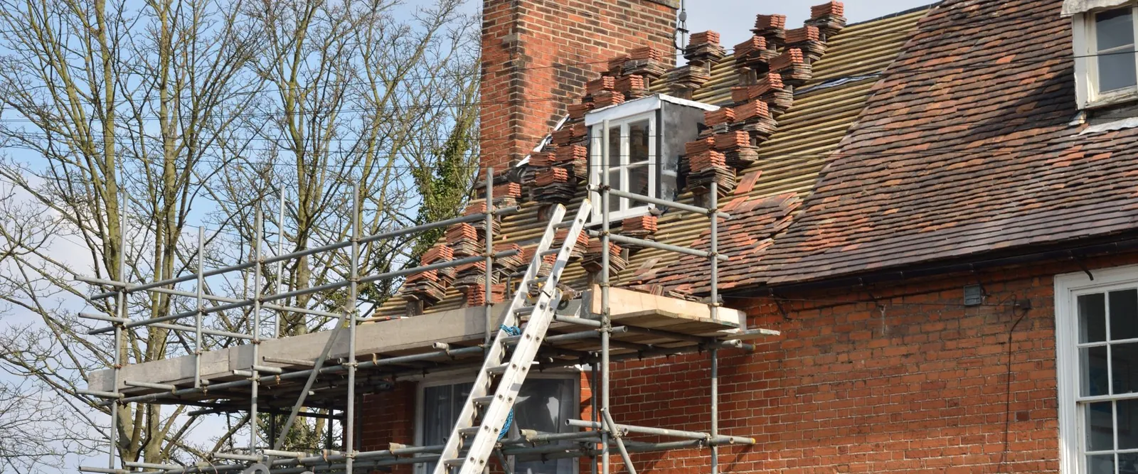 Clay plain tile re-roof in progress with scaffolding on a brick house