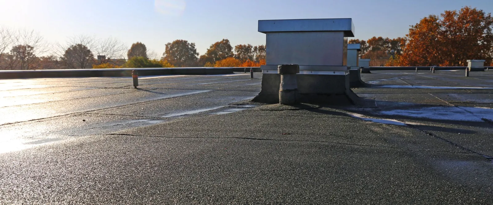 Felt flat roof with vent pipe and plant housing in low sun