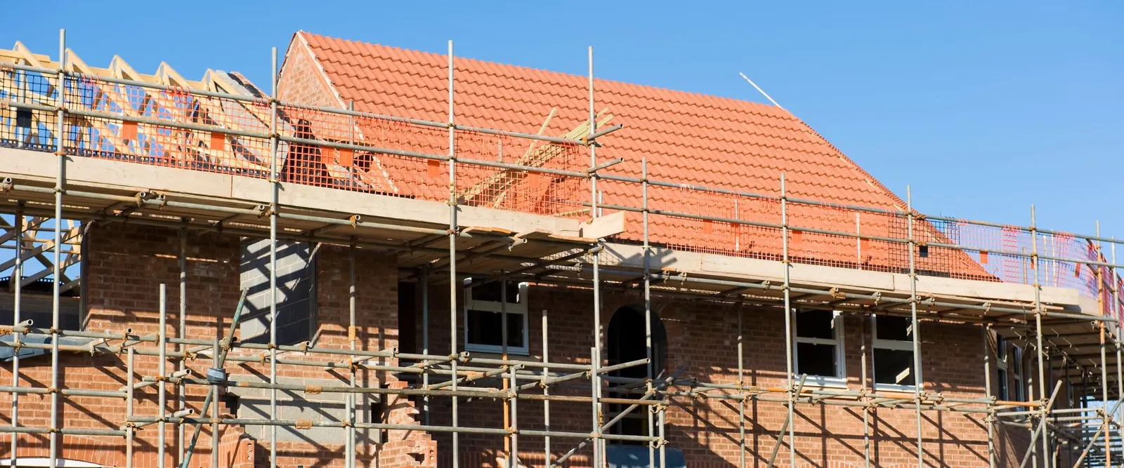 New brick house with a red tiled roof inside scaffolding